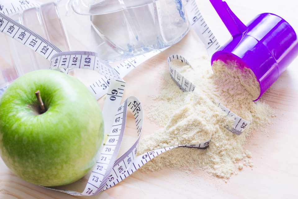 Protein powder and measuring tape|measuring scoop of whey protein powder with a bowl on wooden surface