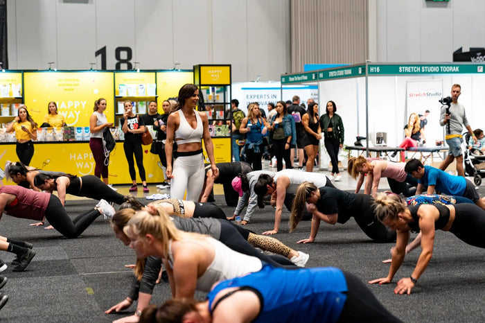 Sophie Guidolin leading a live group training session at a fitness show, with participants performing push-up variations.